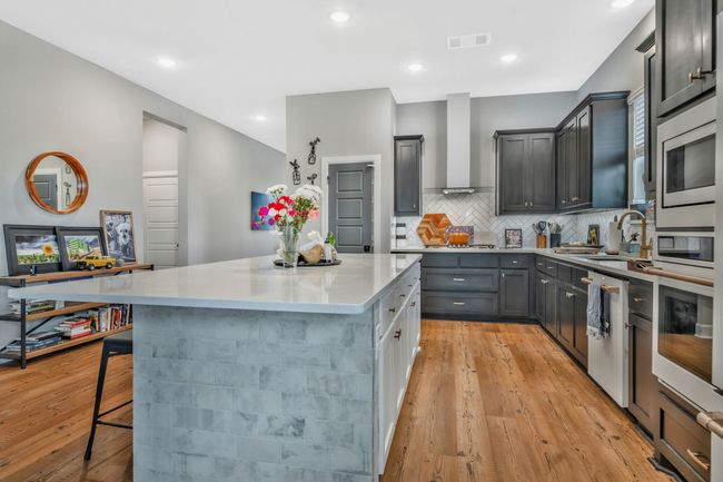 Kitchen with wall chimney range hood, a kitchen island, decorative backsplash, dishwasher, and light wood-style flooring | Image 10