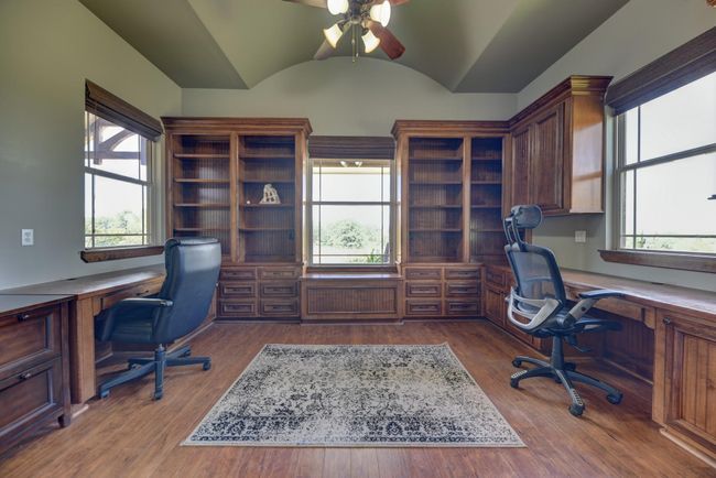Spacious study/home office with built-in wooden shelves and desks, large windows for natural light, and a high ceiling with a fan. Perfect for productivity and storage. | Image 18