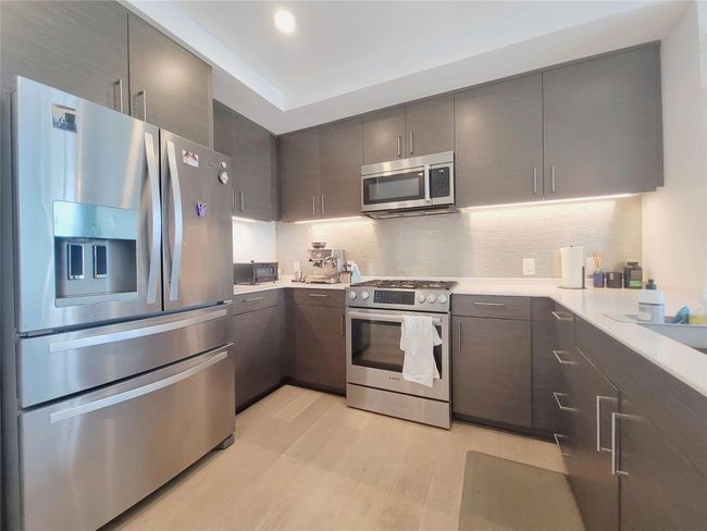 Kitchen featuring stainless steel appliances, light wood-type flooring, light countertops, tasteful backsplash, and modern cabinets | Image 28