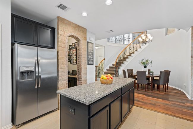 Kitchen featuring stainless steel fridge, a kitchen island, light stone countertops, light tile patterned flooring, and recessed lighting | Image 9