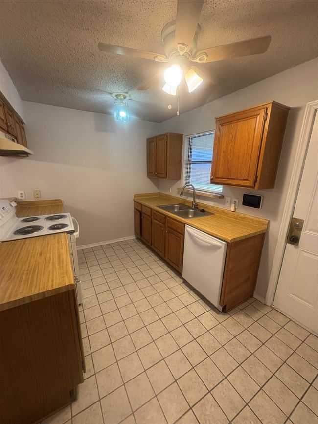 Kitchen featuring light tile patterned flooring, a ceiling fan, a textured ceiling, dishwashing machine, and range | Image 6