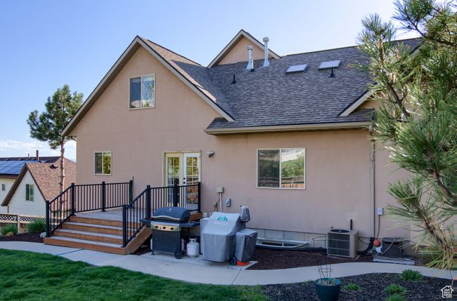 Rear view of house with a wooden deck, central air condition unit, a shingled roof, and stucco siding | Image 43