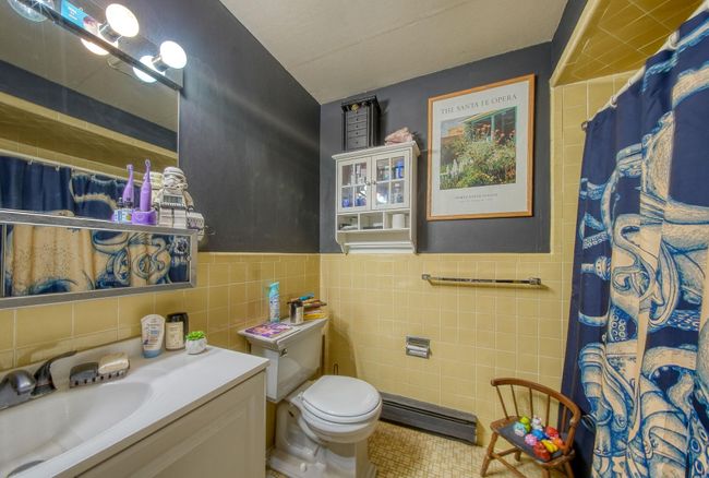 Bathroom with toilet, vanity, a shower with curtain, baseboard heating, and tile walls | Image 10