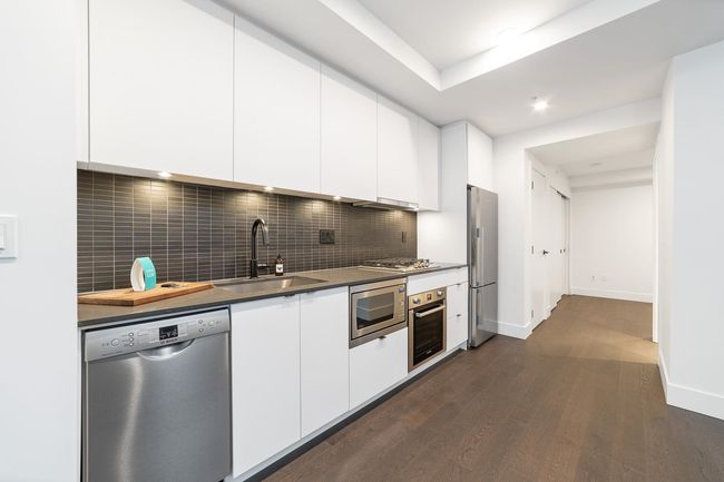 Kitchen with stainless steel appliances, dark wood-style floors, white cabinets, and tasteful backsplash | Image 23