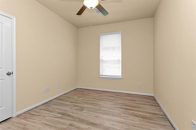 The first secondary bedroom features luxury vinyl plank flooring, a ceiling fan for comfort, and a large window that fills the space with natural light. | Image 17