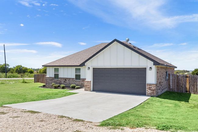 View of front of house featuring brick siding, roof with shingles, board and batten siding, a garage, and concrete driveway | Image 4