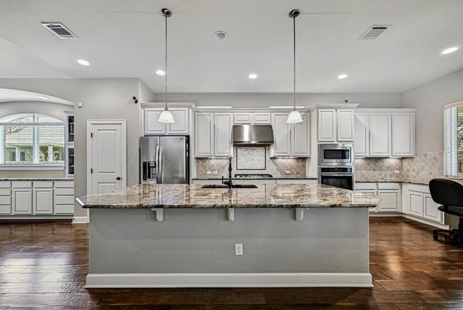 Kitchen with appliances with stainless steel finishes, under cabinet range hood, white cabinets, arched walkways, and light stone countertops | Image 9