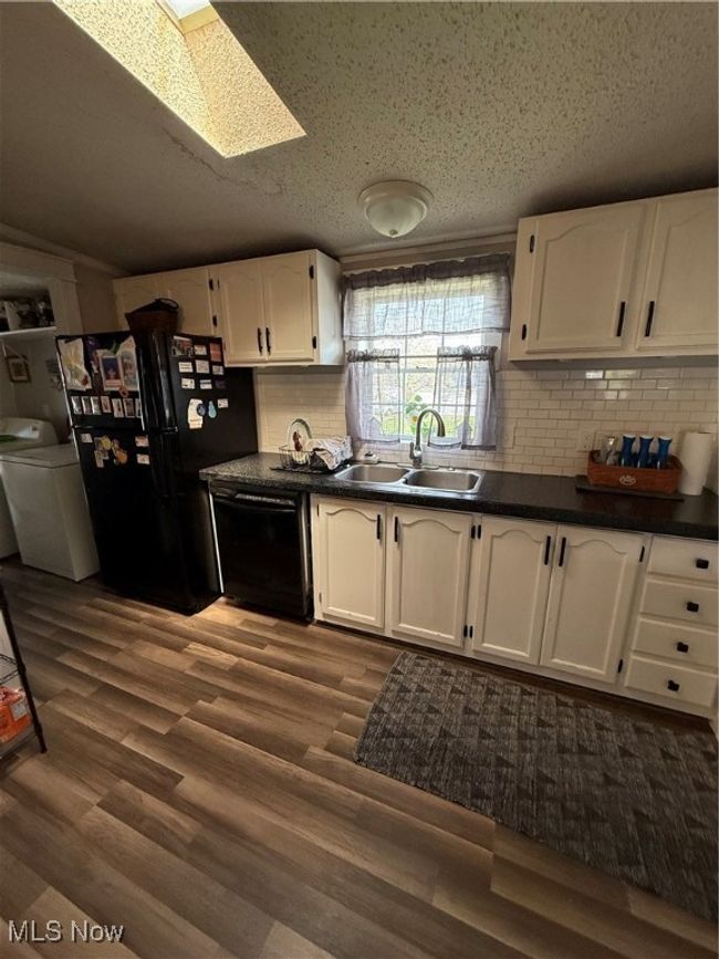 Kitchen featuring a sink, dark countertops, white cabinetry, dishwashing machine, and refrigerator | Image 12