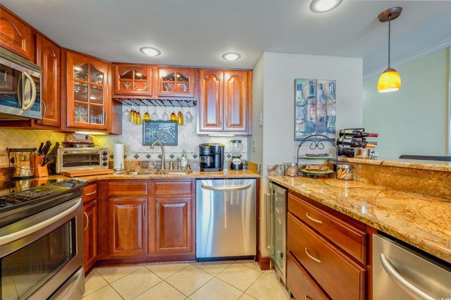 Kitchen featuring stainless steel appliances, a sink, wine cooler, light stone countertops, and backsplash | Image 16