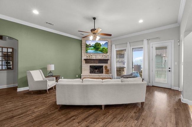 Living room with ceiling fan, a stone fireplace, dark wood finished floors, crown molding, and baseboards | Image 7