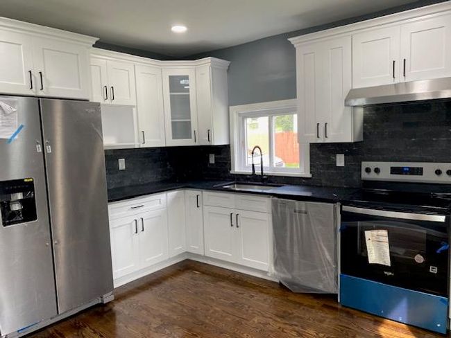 Kitchen featuring stainless steel appliances, dark countertops, dark wood-style floors, under cabinet range hood, and white cabinets | Image 12