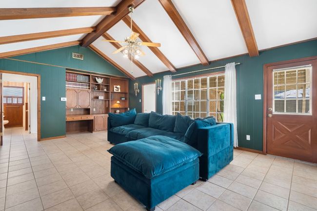 Living room featuring ceiling fan, original wood beams, light tile patterned floors, built-in bookshelves - perfect for a mini library or study area, and accented with wood panel walls | Image 14