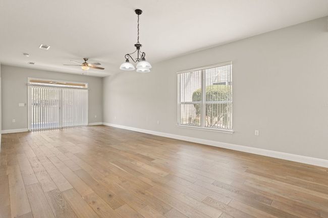 Empty room featuring ceiling fan with notable chandelier, visible vents, light wood-style flooring, and baseboards | Image 12