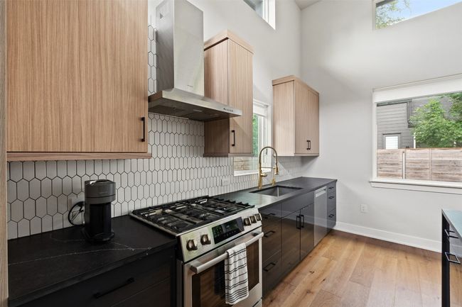 Kitchen featuring gas stove, wall chimney range hood, dark countertops, plenty of natural light, and a towering ceiling | Image 9