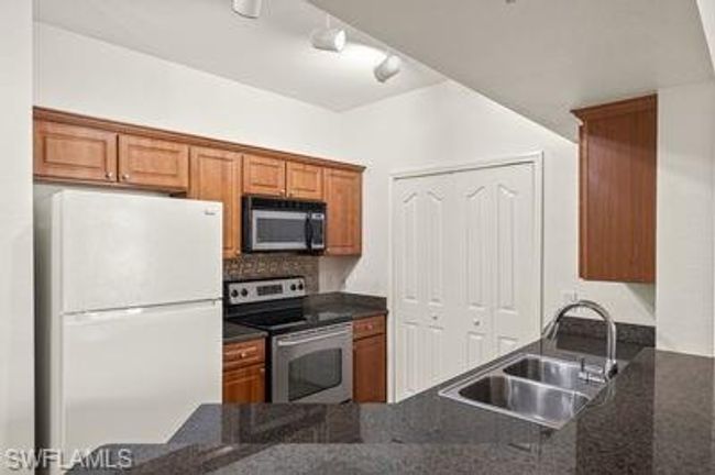 Kitchen featuring a sink, appliances with stainless steel finishes, brown cabinetry, dark stone counters, and decorative backsplash | Image 15