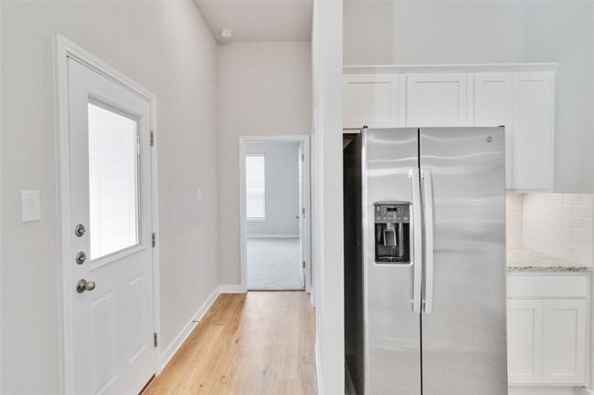 Kitchen featuring stainless steel fridge, white cabinets, decorative backsplash, light wood-style flooring, and light stone counters | Image 26