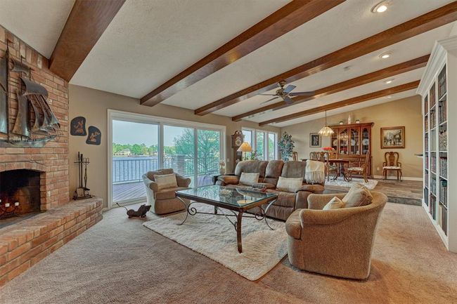 The living room features rustic wood beam accents and a charming corner brick fireplace. Large sliding glass doors and windows frame expansive views of Lake Conroe. | Image 8
