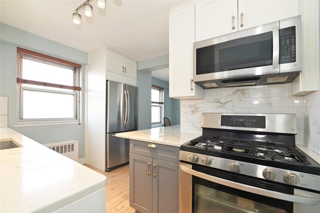 Kitchen featuring stainless steel appliances, radiator, light stone countertops, light wood-style flooring, and tasteful backsplash | Image 6