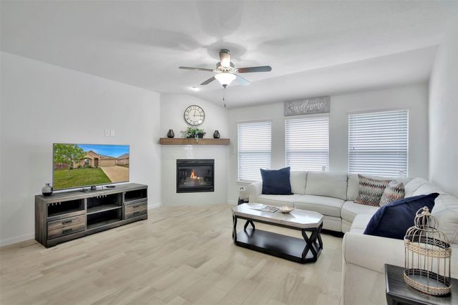 Living room with a glass covered fireplace, a ceiling fan, baseboards, and wood finished floors | Image 10