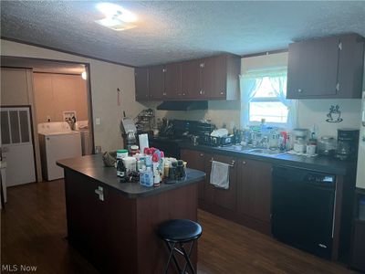 Kitchen featuring black dishwasher, a textured ceiling, independent washer and dryer, dark wood-type flooring, and a center island | Image 3