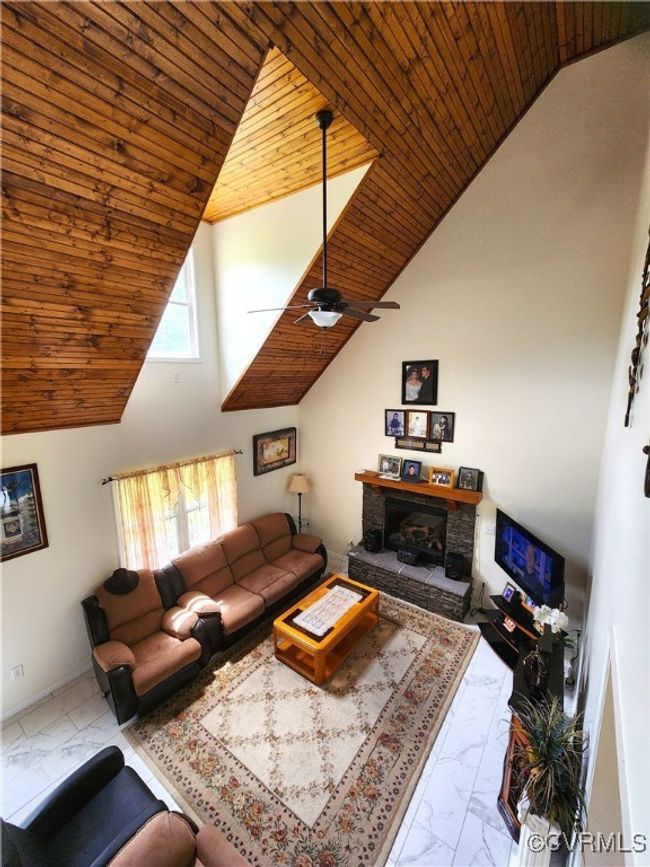 Living area featuring marble finish flooring, wood ceiling, high vaulted ceiling, a fireplace, and a ceiling fan | Image 6