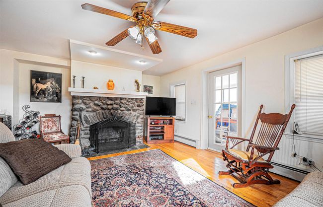 Living room featuring a stone fireplace, ceiling fan, light hardwood / wood-style flooring, and a baseboard radiator | Image 7