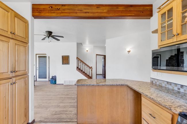 Kitchen with a peninsula, ceiling fan, beamed ceiling, light stone countertops, and light wood finished floors | Image 25