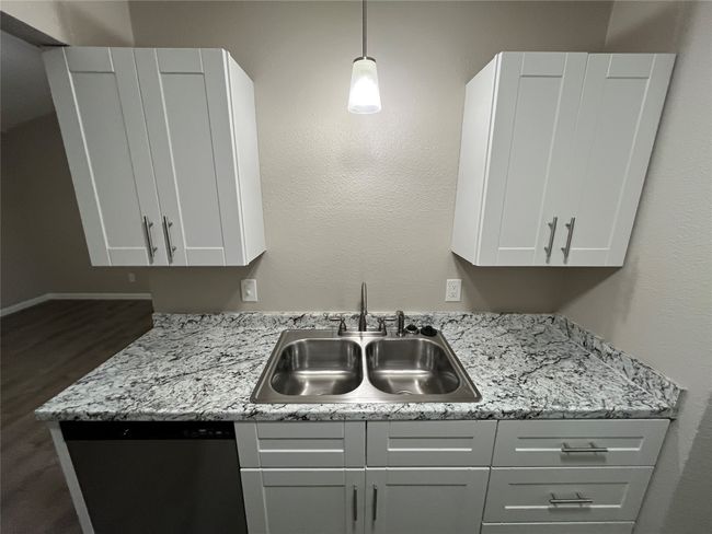 Kitchen with a sink, stainless steel dishwasher, dark wood finished floors, pendant lighting, and white cabinets | Image 7