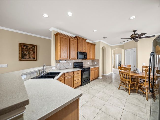 Kitchen featuring arched walkways, a sink, light countertops, decorative backsplash, and black appliances | Image 10