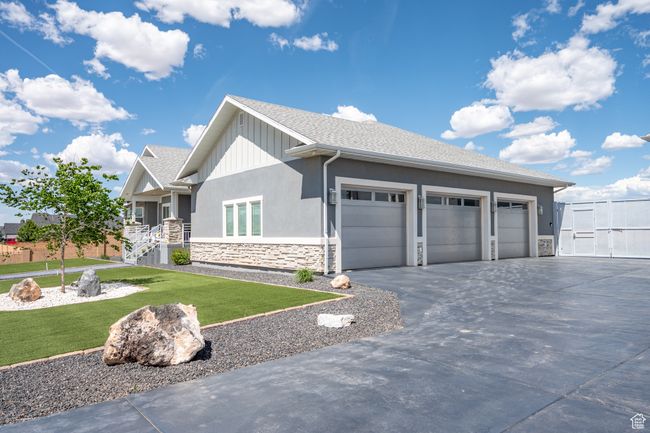 View of home's exterior featuring stone siding, concrete driveway, a lawn, a garage, and stucco siding | Image 107