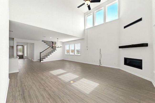 Unfurnished living room featuring healthy amount of natural light, a glass covered fireplace, ceiling fan, a high ceiling, and stairway | Image 5