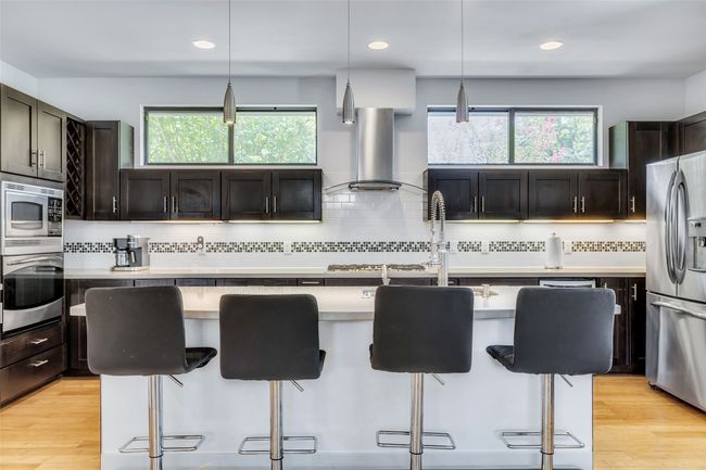 Kitchen with an island with sink, a kitchen bar, hanging light fixtures, and appliances with stainless steel finishes | Image 7