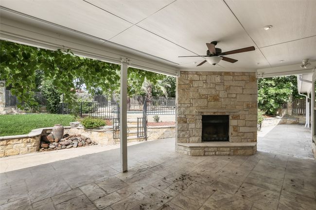 Fenced backyard with an outdoor stone fireplace, a ceiling fan, and a patio area | Image 16