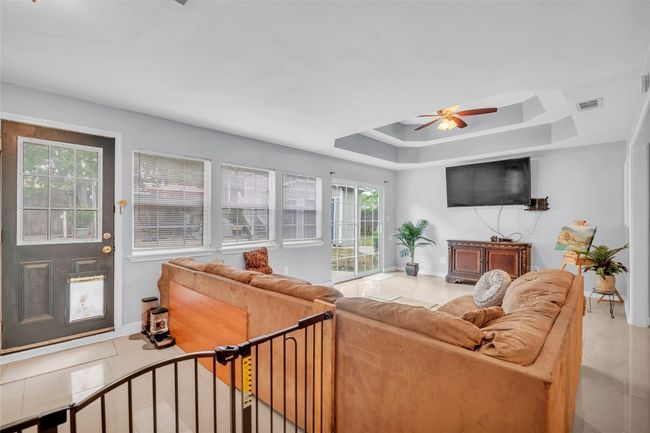 Living area with visible vents, baseboards, tile patterned floors, a tray ceiling, and a ceiling fan | Image 26