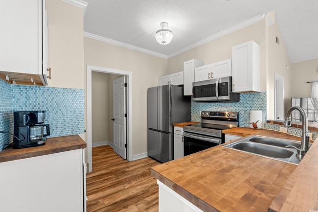 Kitchen featuring a sink, appliances with stainless steel finishes, wooden counters, light wood-type flooring, and white cabinets | Image 9