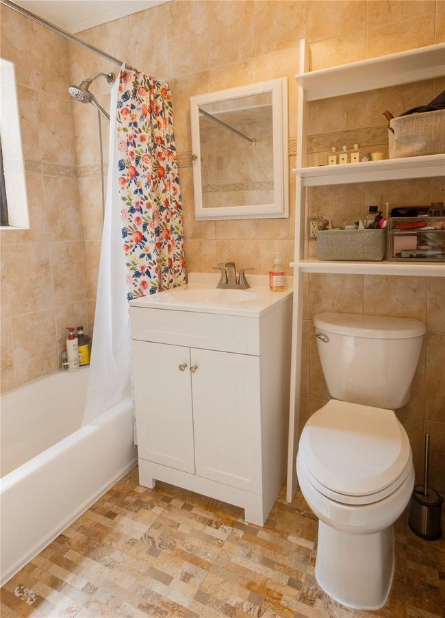 Bathroom with tile walls, toilet, shower / bath combo with shower curtain, and vanity | Image 16
