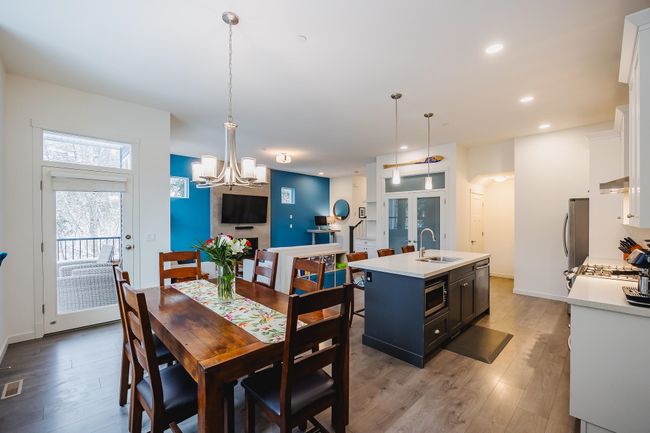 Kitchen with wood finished floors, a sink, a kitchen island with sink, light countertops, and a fireplace | Image 10