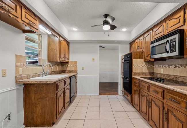 Kitchen with black appliances, a sink, a textured ceiling, ceiling fan, and backsplash | Image 12