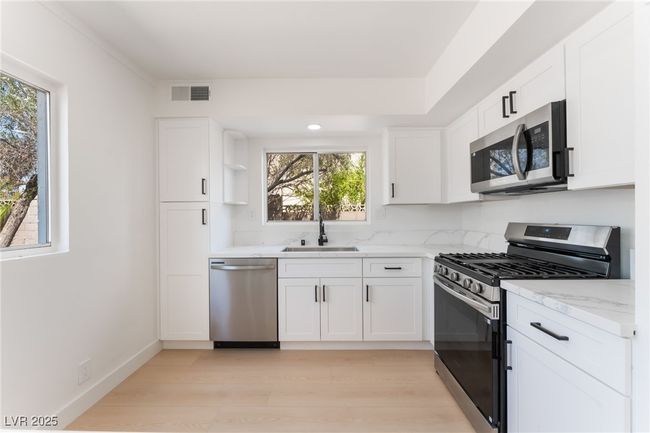 Kitchen with stainless steel appliances, open shelves, light wood-style flooring, light stone countertops, and white cabinets | Image 16