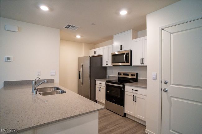 Kitchen with appliances with stainless steel finishes, a peninsula, light wood finished floors, white cabinets, and light stone countertops | Image 4