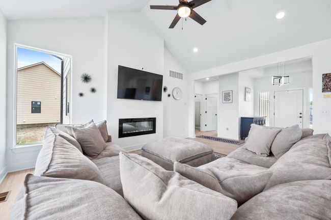 Living area featuring high vaulted ceiling, a ceiling fan, a glass covered fireplace, light wood-style floors, and baseboards | Image 9