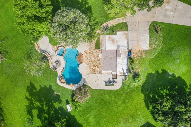 This aerial photo showcases a beautifully landscaped backyard centered around a custom-designed pool area. The pool features a freeform shape with natural stone coping, a connected raised spa, and a built-in gas fire pit nearby—perfect for outdoor entertaining. | Image 6