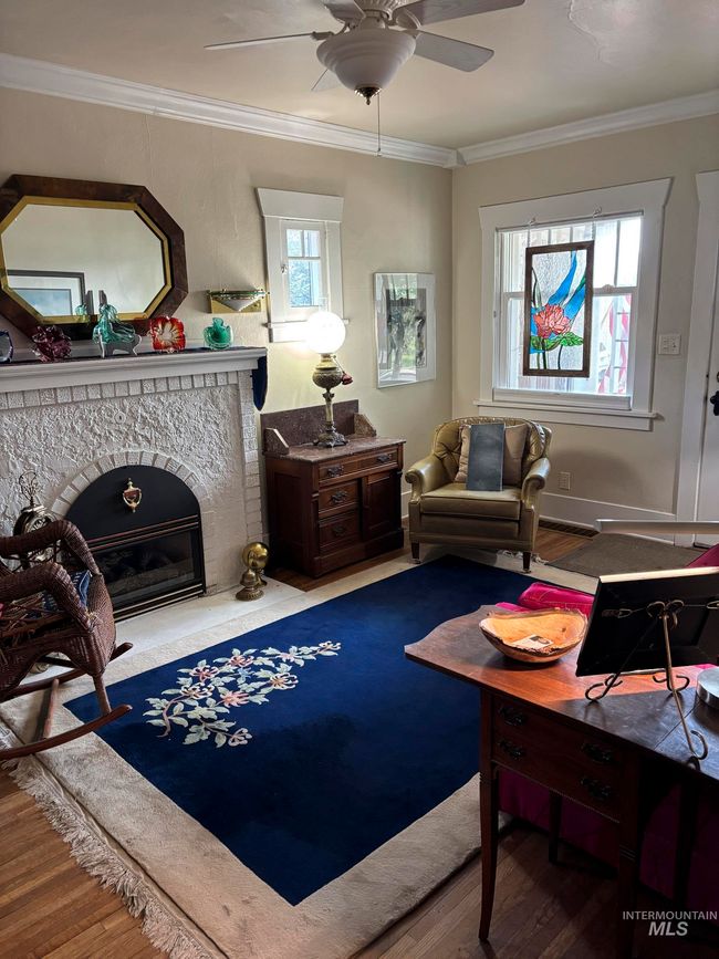 Living area with wood finished floors, a ceiling fan, ornamental molding, and a fireplace | Image 9