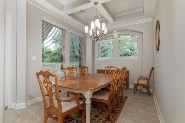 This elegant formal dining room features a coffered ceiling, a stylish chandelier, and large windows for natural light. The space is complemented by the neutral-toned walls, creating a warm and inviting atmosphere. | Image 22