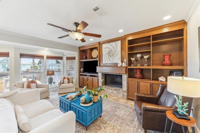 This cozy living room features a warm, inviting atmosphere with a fireplace, built-in wooden shelves, and ample natural light from large windows. Comfortable seating and tasteful decor create a perfect space for relaxation or entertaining. | Image 10