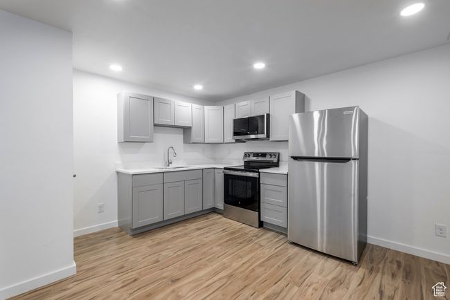 Basement kitchen with light wood-style floors, gray cabinets, a sink, and appliances with stainless steel finishes | Image 28