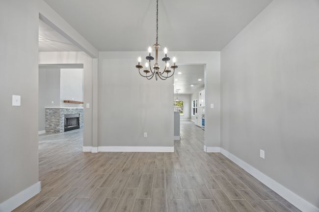 Unfurnished dining area with a fireplace, light wood-style flooring, baseboards, and an inviting chandelier | Image 5