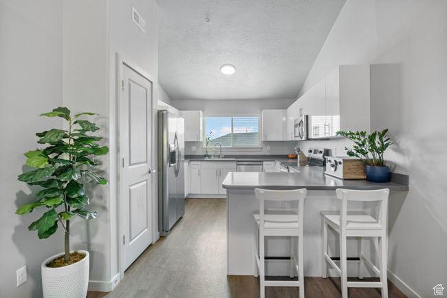 Kitchen featuring visible vents, a peninsula, stainless steel appliances, a sink, and light wood-type flooring | Image 14