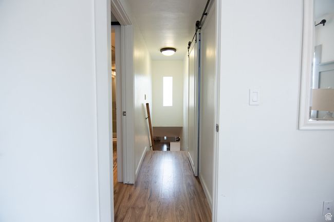 Corridor with a barn door, wood finished floors, an upstairs landing, and baseboards | Image 25