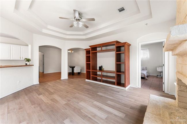 Unfurnished living room with a tray ceiling, arched walkways, a ceiling fan, and light wood-style flooring | Image 15
